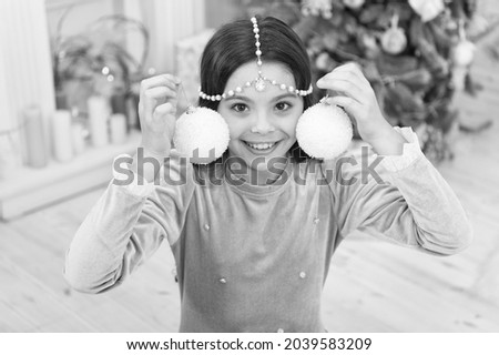 Dreams come true. Christmas decorating ideas. Child smiling girl hold christmas ornament. Adorable cheerful girl making wish near christmas tree decorated interior. Playful mood. New year eve