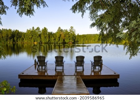 Wet wooden dock with four muskoka chairs facing the lake