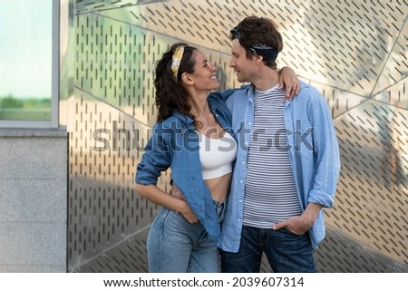 Couple of young hipsters wearing trendy denim jeans clothes and hippie bandana looking at each other happy smiling. Portrait of stylish man and woman millennials dressed in urban style outfit outdoors
