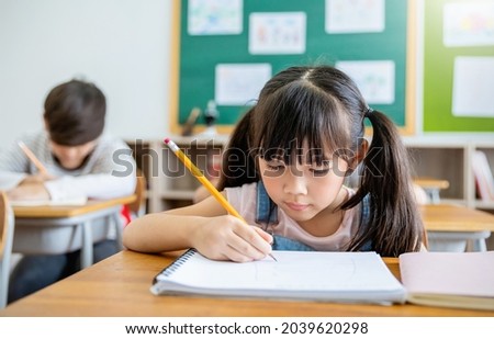 Portrait of little pupil writing at desk in classroom at the elementary school. Student girl study doing test in primary school. Children writing notes in classroom. Education knowledge concept Royalty-Free Stock Photo #2039620298