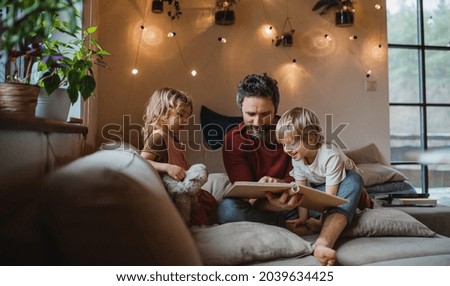 Mature father with two small children resting indoors at home, looking at photo album. Royalty-Free Stock Photo #2039634425