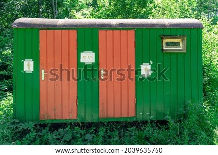 Old green construction trailer converted into a public toilet in the forest