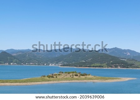 There are some small islands in the middle of the blue sky and the blue lake. There are green trees by the lake
