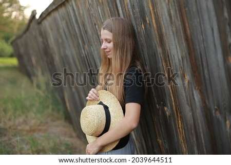 Girl in a straw hat near a brown wooden fence.