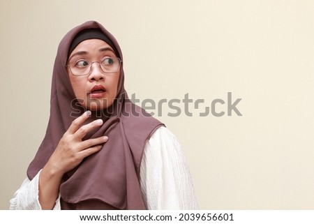 An Asian Muslim woman looking back over her shoulder with surprise expression.