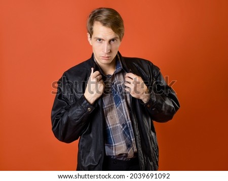 a guy in a casual plaid shirt and a leather jacket, studio photo on an orange background. simple American guy.