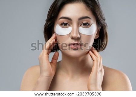 Beautiful brunette woman with a smooth skin applying adhesive under-eyes patches for dark circles 