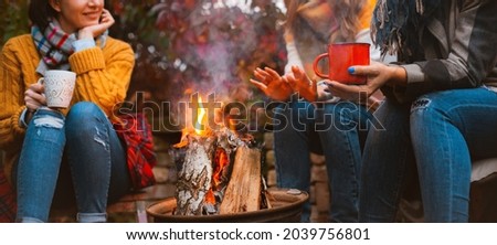 Three females best friends sitting around bonfire in casual clothes warming up and communicating