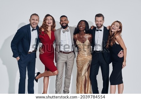 Group of beautiful people in formalwear bonding and smiling while standing against gray background Royalty-Free Stock Photo #2039784554