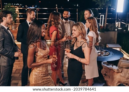 Group of beautiful young people in formalwear communicating and smiling while spending time on luxury party Royalty-Free Stock Photo #2039784641