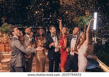 Group of happy people in formalwear having fun together with confetti flying all around Royalty-Free Stock Photo #2039784692