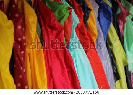 Many wet children's raincoats of different colors are hanging on hangers to get dry again. This picture proes that also rainy day can be happy and colorful, raincoats together looks like a rainbow.