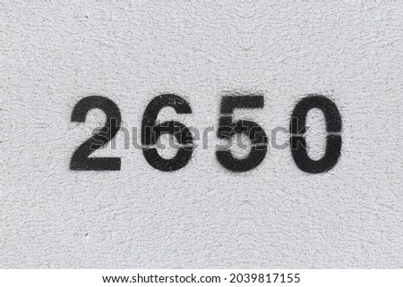 Black Number 2650 on the white wall. Spray paint. Number two thousand six hundred fifty.