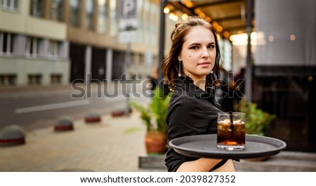 young waitress standing in outdoor cafe. girl the waiter holds a tray with a glass of alcoholic cocktail Royalty-Free Stock Photo #2039827352
