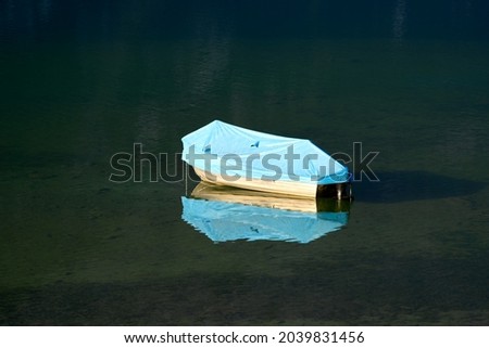 Moored boat with blue cover at Lake Klöntal at a beautiful late summer morning with reflections in calm water. Photo taken September 4th, 2021, Klöntal, Switzerland.