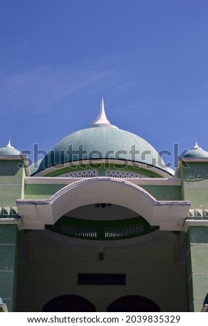 front view photo of a green and white mosque where Muslim prayer is located in East Java, Indonesia with a beautiful blue sky. Horizontal photography layout used for Ramadan eid concept background