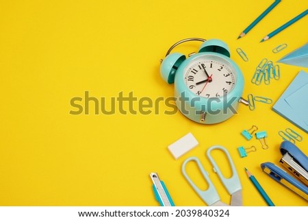 Blue clock with various devices placed on a yellow background.