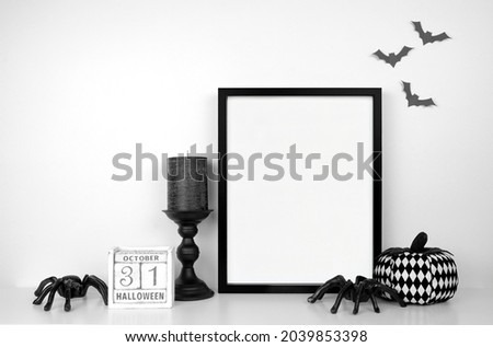Halloween mock up. Black frame on a white shelf with black and white decor. Portrait frame against a white wall with bats. Copy space.