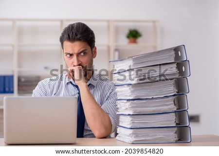 Young male employee and too much work in the office Royalty-Free Stock Photo #2039854820
