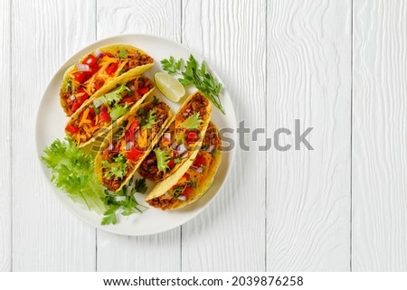 Ground Beef Tacos with shredded cheddar cheese, fresh lettuce, tomato, onion on a white plate with lime wedges, horizontal view from above, mexican cuisine, flat lay, free space