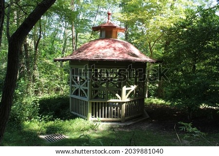 Photograph of wooden gazebo in the woods with trees in a natural setting.