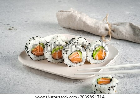 A set of fresh sushi rolls with salmon, avocado and black sesame seeds served on a plate with chopsticks. Japanese sushi uramaki or California roll