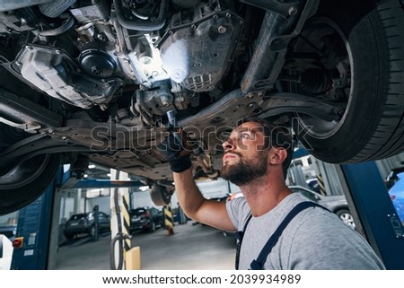 Male with flashlight below automobile studying its underside Royalty-Free Stock Photo #2039934989