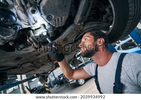 Automobile repairman examining car underside using flashlight Royalty-Free Stock Photo #2039934992