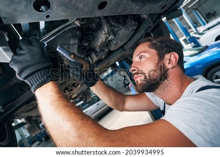 Mechanic is inspecting car underside with flashlight Royalty-Free Stock Photo #2039934995