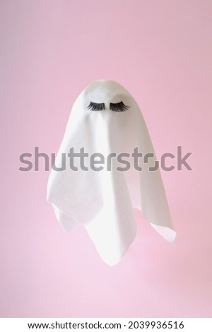 White ghost with lashes on a pink background. Halloween scary background. Minimal composition
