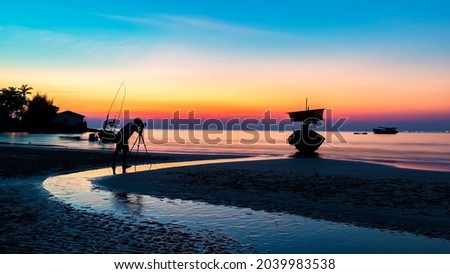 Silhouette of a photographer, taking the beautiful moments during the sunset at have water reflection light. 