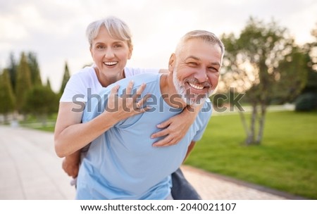 Portrait of lovely happy elderly couple on morning run outside in city park, retirees wife and husband rejoice in active lifestyle, smiling woman tenderly embracing her spouse after routine jogging Royalty-Free Stock Photo #2040021107