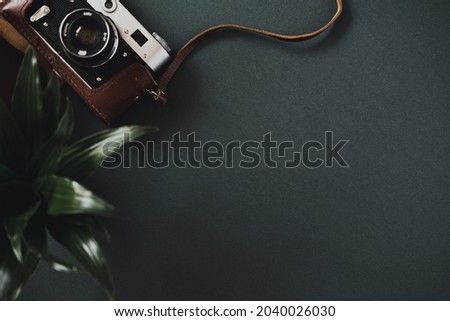 Top view of a flat lay film camera in a case lies on a black table next to a plant in a pot. Concept of workspace of a photographer or amateur. Advertising space