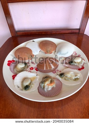 A picture of a type of shell called a scallop whose skin has been opened on a ceramic plate
