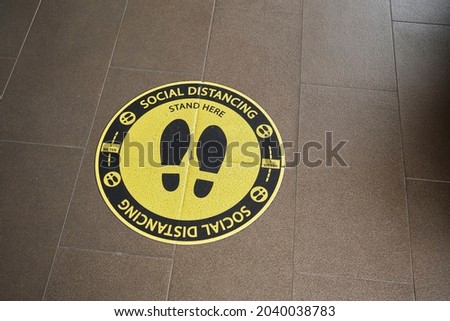 Yellow and black colored logo of 1 meter social distancing with shoe soles on the floor