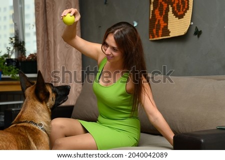 Photo of a woman playing with a ball smiling with a belgian shepherd malinois sitting on a sofa at home