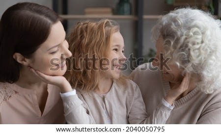 Adorable small kid girl communicating with beautiful young mum and middle aged elderly grandmother, talking chatting spending free weekend leisure time together at home, family relations concept.