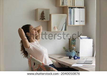 Happy smiling young woman stretching leaned on comfy chair hold hands behind head finished study breath fresh air sit at home office desk feel satisfaction enjoy break after work done daydream concept Royalty-Free Stock Photo #2040050876