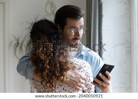 Young husband hugs wife holds cellphone check messages in social media suspect her in treason. Broken trust in relationships, jealous boyfriend, mistrust in relations, crisis of family life concept Royalty-Free Stock Photo #2040050921
