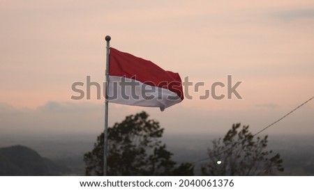 The red and white Indonesian flag flutters against the background of the evening sky approaching evening. This photo was taken on top of the mountain