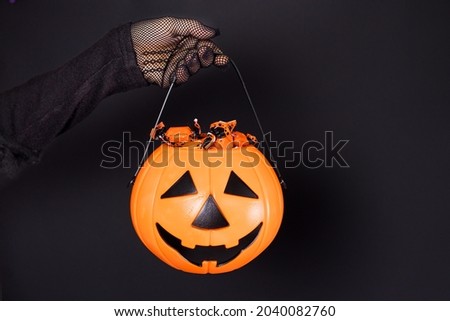 A bucket of candy in the form of a pumpkin lantern Jack on a black background in a hand in a mesh glove. Accessories for Halloween.