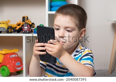 A little boy 3-4 years old looks into the phone screen. Cartoons for children, screen time, children's dependence on the computer and phone