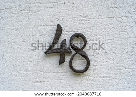 Metal house number 48 on a white stucco wall background, close up