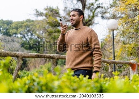 young hispanic latino man sending audio on his smart cell phone in a city park