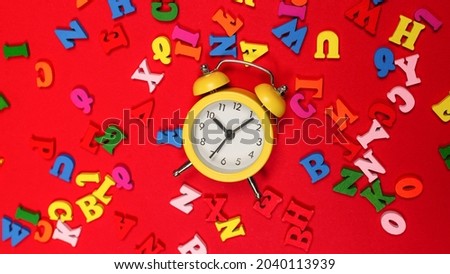 Random colorful alphabet and yellow alarm clock on a red background, colorful letters. Time to school. Study time. Education time.