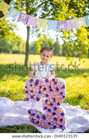 Cheerful girl having fun on child birthday on blanket with paper decorations in the park. High quality photo