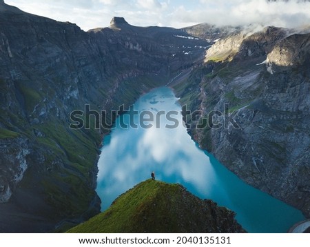 Adventurous man is standing on top of the mountain ridge and enjoying the beautiful view during a vibrant sunset. Beautiful Switzerland landscape aerial photography, Limmernsee Lake, Muttsee, Glarus