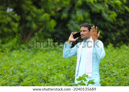 Indian farmer talking on smartphone at green agriculture field