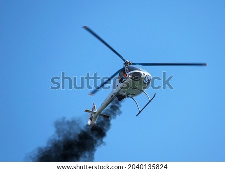 Helicopter with engine problems. Black smoke comes out of the helicopter's engine and the helicopter tries to make an emergency landing. Small helicopter. Royalty-Free Stock Photo #2040135824