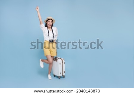 Happy young Asian tourist woman holding baggage going to travel on holidays isolated on blue background. Royalty-Free Stock Photo #2040143873